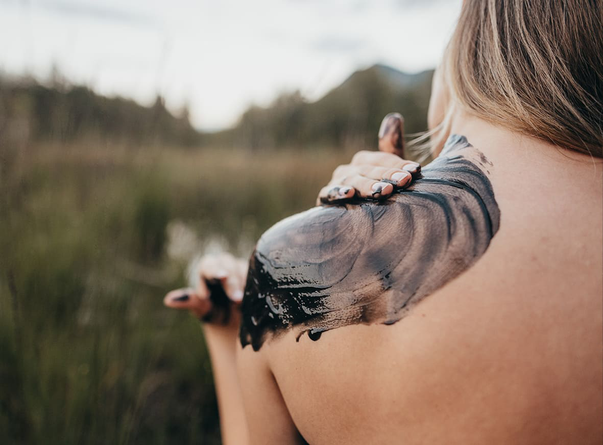Frau in der Natur verteilt Hautpflegeprodukt auf die Schulter